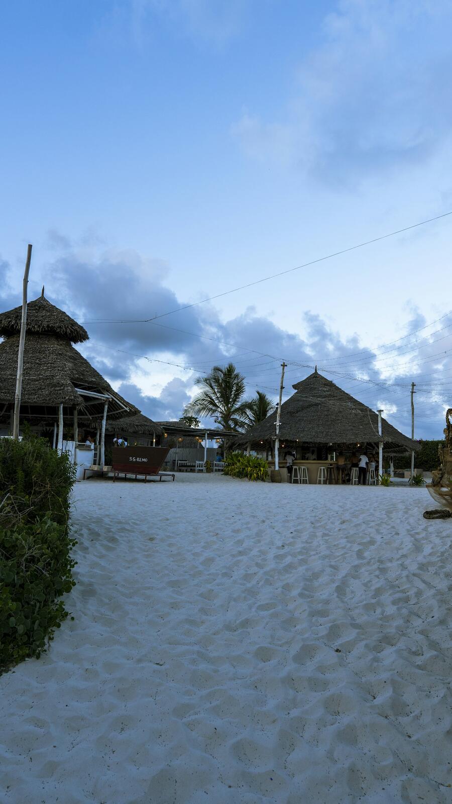 a sandy path leading to a beach with thatched huts — illustrative property style — illustrative style for Nairobi Garden Court