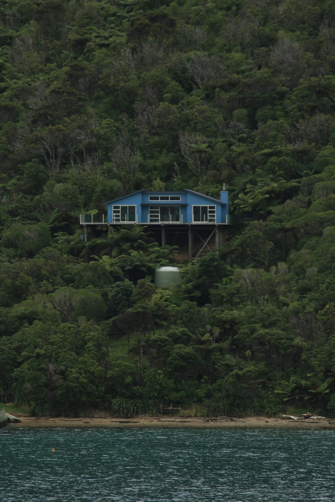 Blue house nestled on a lush green hillside — illustrative property style — illustrative style for Abel Tasman Coastal Villas