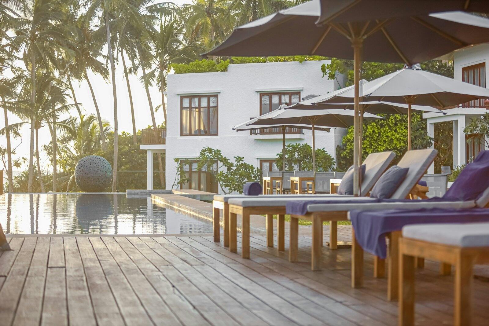 A wooden deck with chairs and umbrellas next to a swimming pool — illustrative property style — illustrative style for Wildwood Safari Lodge