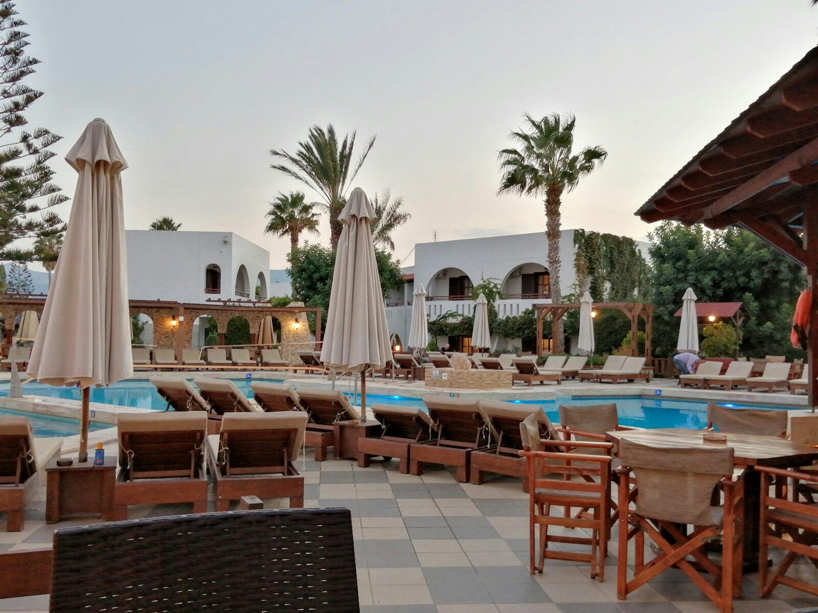 an outdoor pool with tables and chairs and umbrellas — illustrative property style — illustrative style for Athens Garden Rooms